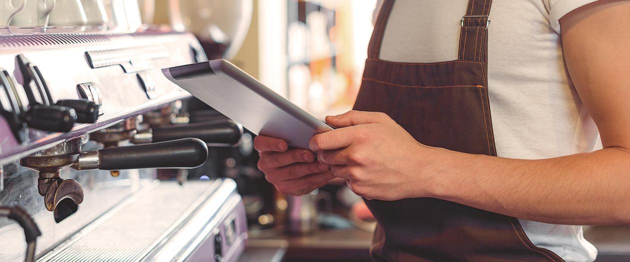 barista on tablet in front of commercial espresso machine